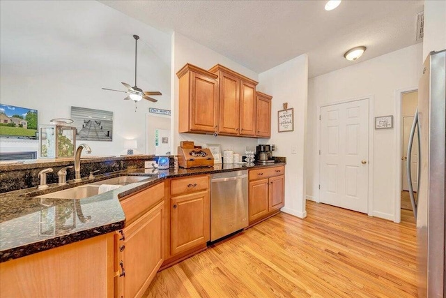 kitchen featuring dark stone countertops, stainless steel appliances, light wood-type flooring, and a sink