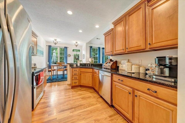 kitchen featuring stainless steel appliances, light wood-style flooring, a sink, a textured ceiling, and a peninsula