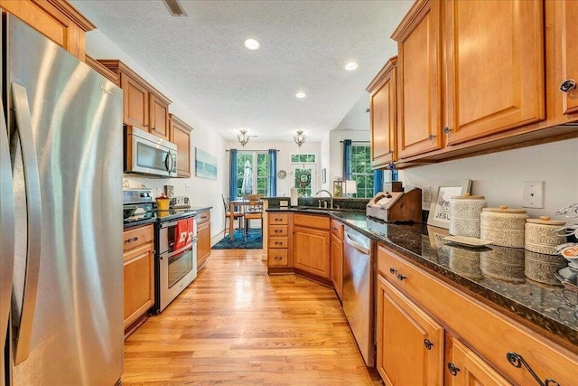 kitchen with a peninsula, light wood finished floors, appliances with stainless steel finishes, and brown cabinetry