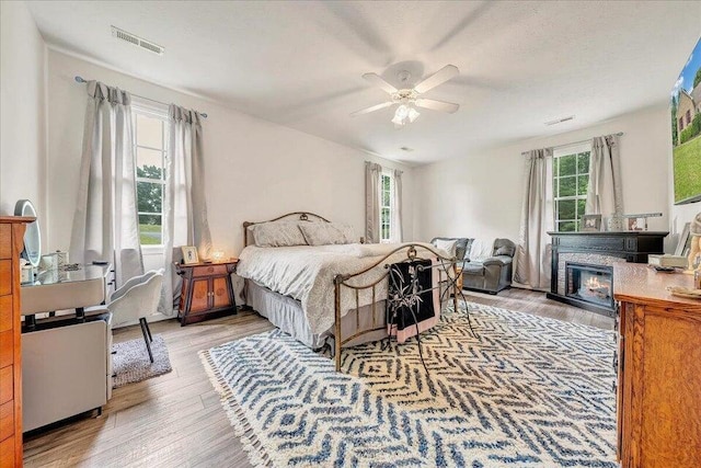 bedroom featuring a glass covered fireplace, wood finished floors, visible vents, and a ceiling fan