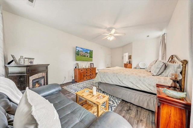 bedroom featuring visible vents, a ceiling fan, wood finished floors, and a glass covered fireplace