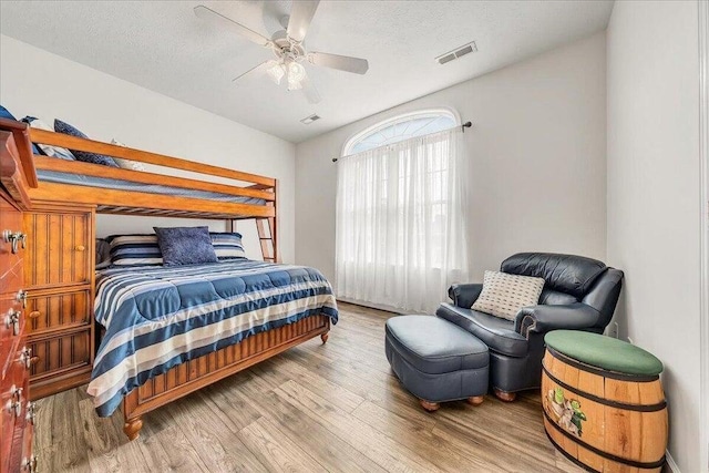 bedroom with a ceiling fan, visible vents, a textured ceiling, and wood finished floors