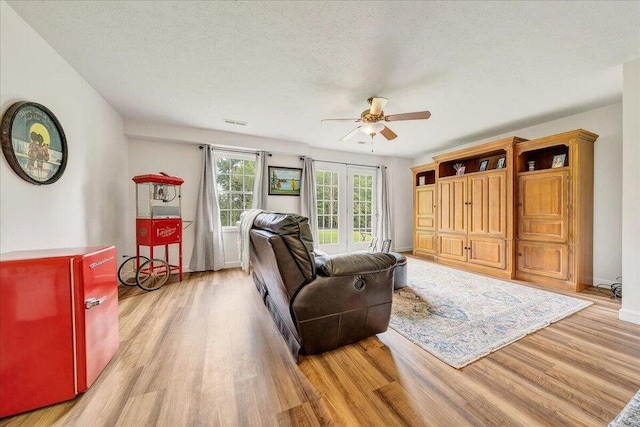 living area with light wood-type flooring, baseboards, a ceiling fan, and a textured ceiling