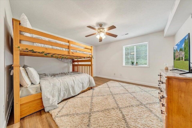 bedroom featuring baseboards, a textured ceiling, visible vents, and wood finished floors