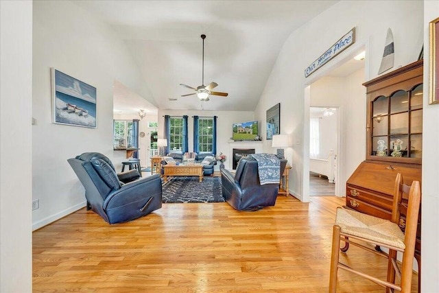 living area featuring light wood-style flooring, a fireplace, vaulted ceiling, and a ceiling fan