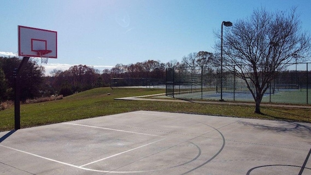 view of sport court with a tennis court, community basketball court, a lawn, and fence