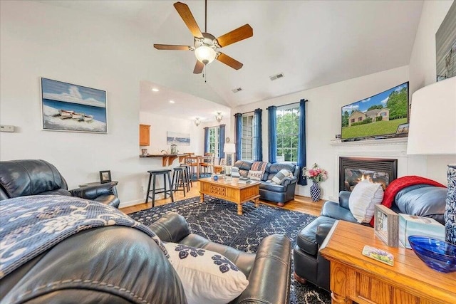 living room with visible vents, a glass covered fireplace, ceiling fan, vaulted ceiling, and wood finished floors