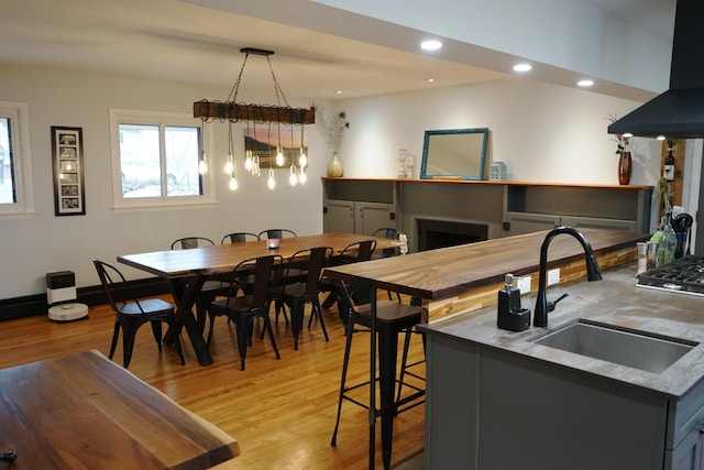 kitchen with recessed lighting, a fireplace, a sink, wall chimney range hood, and light wood finished floors