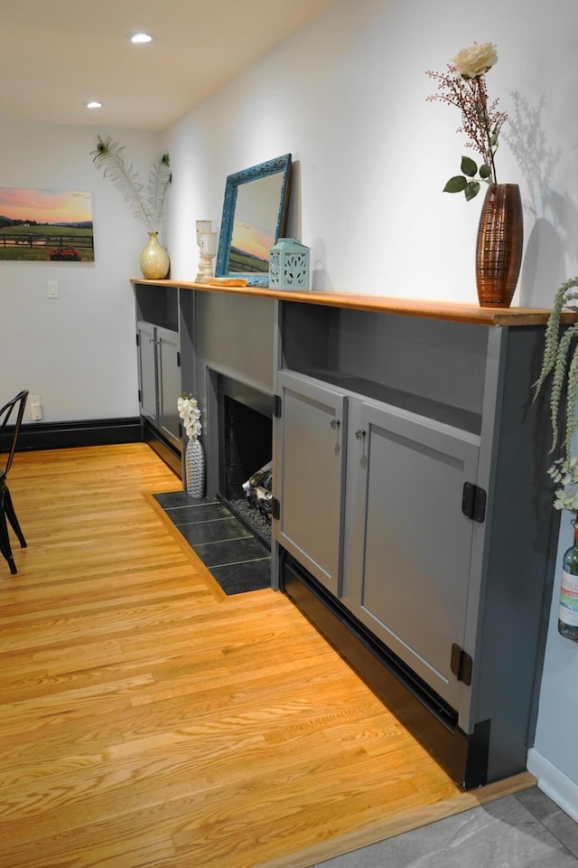 interior space with a fireplace with flush hearth, recessed lighting, light wood-style flooring, and baseboards