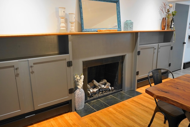 interior details featuring a fireplace with flush hearth, a baseboard heating unit, and wood finished floors