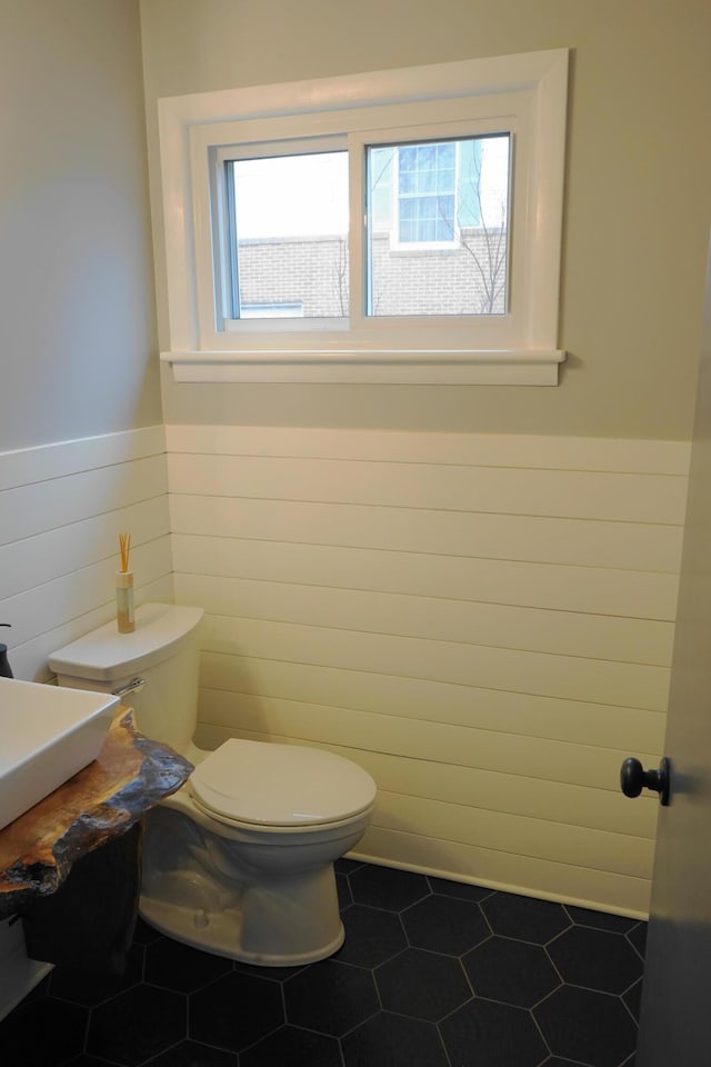 half bathroom featuring toilet, a wainscoted wall, and tile patterned floors