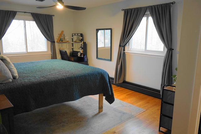 bedroom featuring a baseboard heating unit, ceiling fan, and wood finished floors