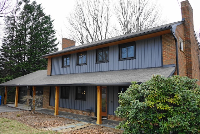 view of front of house with a chimney, a porch, board and batten siding, and brick siding