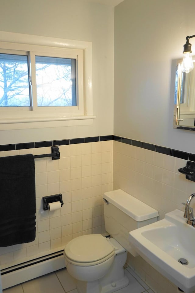 half bathroom with tile patterned flooring, toilet, a baseboard heating unit, a sink, and tile walls