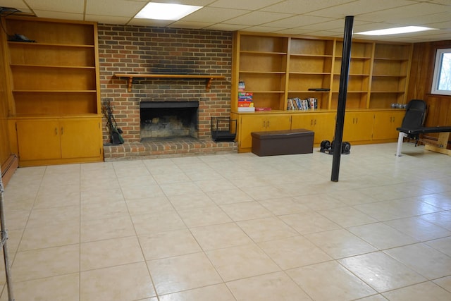 below grade area featuring wood walls, a fireplace, built in features, and a drop ceiling