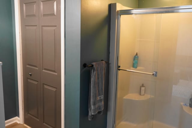 bathroom with a closet, a shower stall, and baseboards