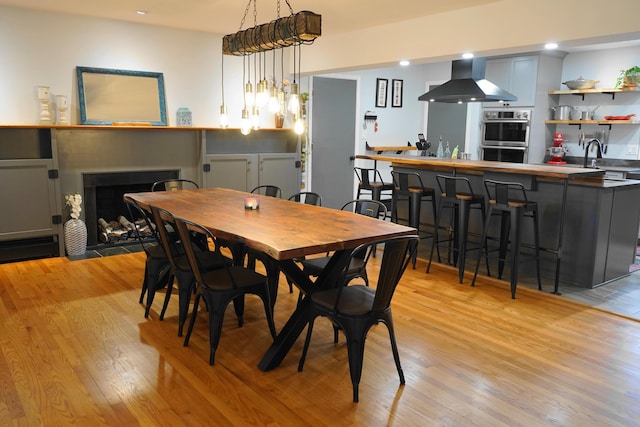 dining space with a fireplace with flush hearth, recessed lighting, indoor wet bar, and light wood-style floors