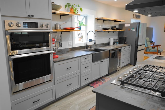 kitchen featuring open shelves, appliances with stainless steel finishes, wall chimney exhaust hood, and a sink