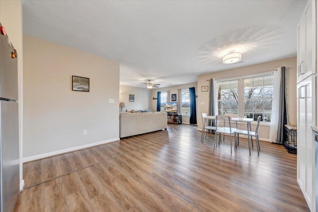 unfurnished living room with baseboards, wood finished floors, a ceiling fan, and a healthy amount of sunlight