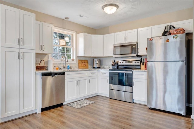 kitchen with light stone counters, appliances with stainless steel finishes, light wood-style floors, white cabinetry, and a sink