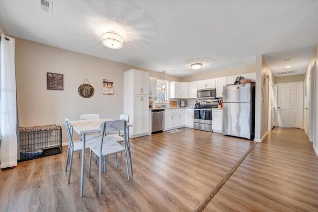 dining space featuring light wood-style floors, visible vents, and baseboards