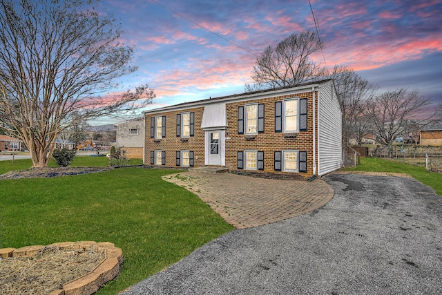 bi-level home with driveway, brick siding, a lawn, and fence