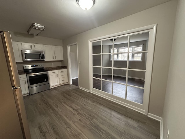 kitchen featuring baseboards, dark countertops, dark wood-style flooring, stainless steel appliances, and white cabinetry