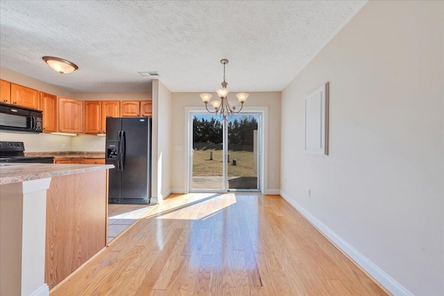 kitchen with visible vents, black appliances, light wood-style floors, an inviting chandelier, and light countertops