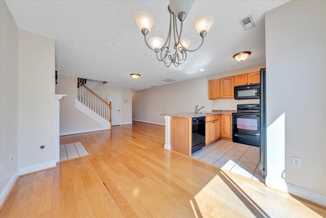 kitchen with black appliances, light countertops, light wood-type flooring, and a peninsula