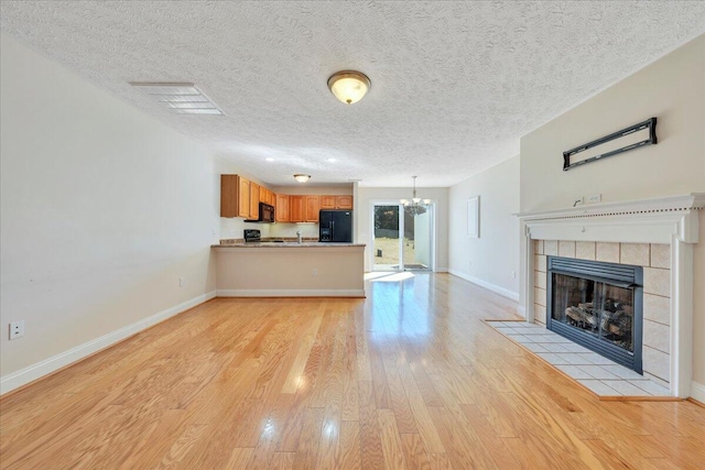 unfurnished living room featuring visible vents, baseboards, a tiled fireplace, an inviting chandelier, and light wood-style floors