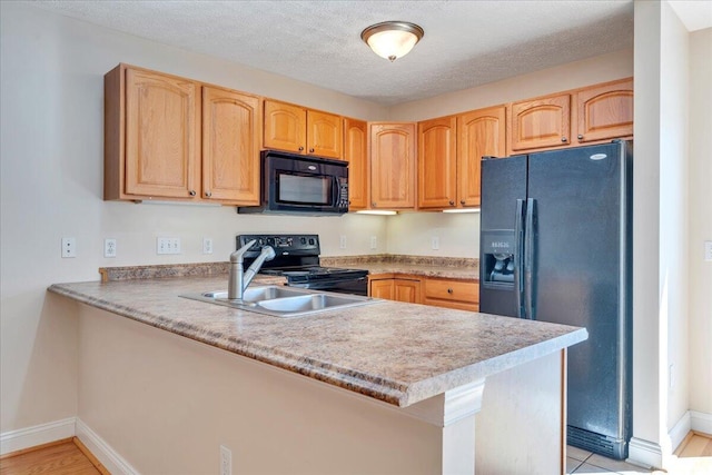 kitchen featuring black appliances, a peninsula, light countertops, and a sink