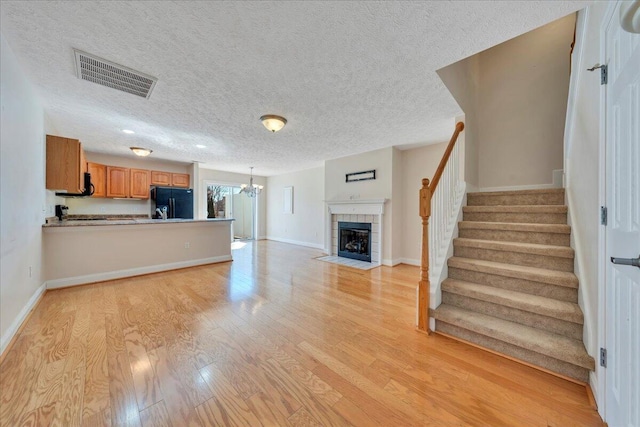 unfurnished living room featuring visible vents, a notable chandelier, light wood-style flooring, a fireplace, and stairs