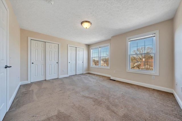 unfurnished bedroom featuring visible vents, baseboards, carpet, multiple closets, and a textured ceiling