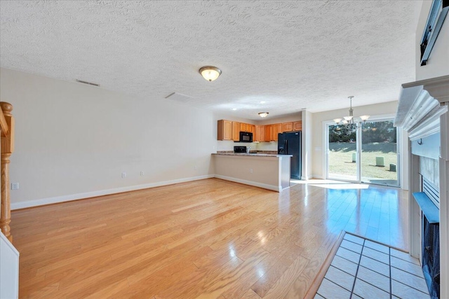 unfurnished living room with visible vents, a fireplace with flush hearth, light wood finished floors, baseboards, and a chandelier