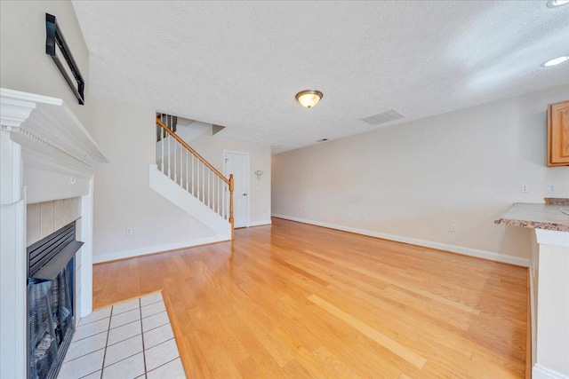 unfurnished living room featuring light wood-type flooring, baseboards, a fireplace, and stairs