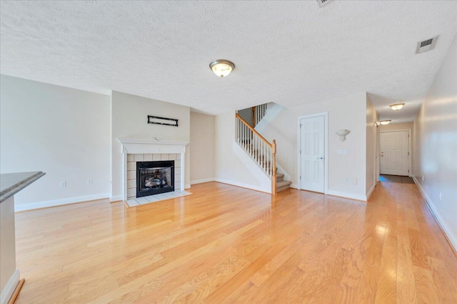 unfurnished living room featuring visible vents, baseboards, stairway, a fireplace, and light wood-style floors