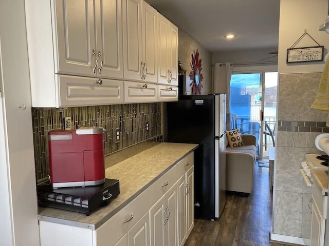 kitchen featuring decorative backsplash, white cabinets, freestanding refrigerator, and dark wood-style floors