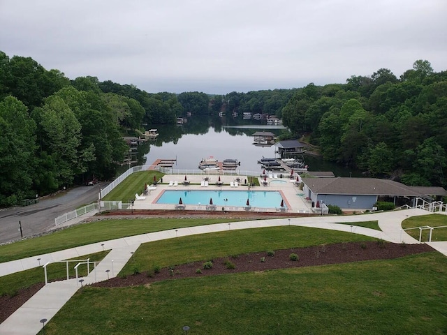 view of pool featuring a lawn, a water view, and a view of trees
