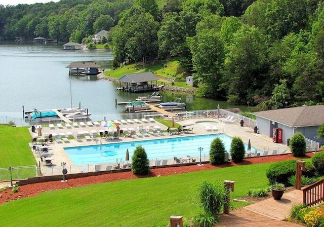 pool with a water view, a view of trees, fence, and a yard