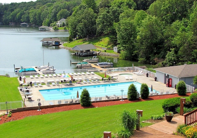 pool featuring a lawn, a patio, a view of trees, fence, and a water view