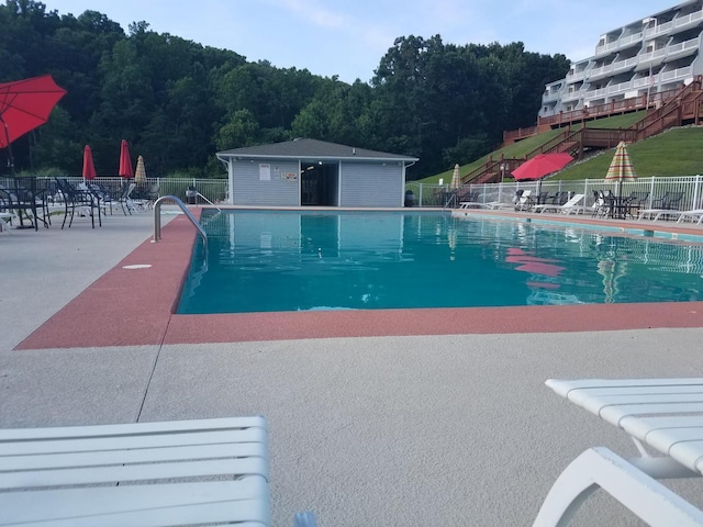 community pool featuring a view of trees, fence, and a patio area