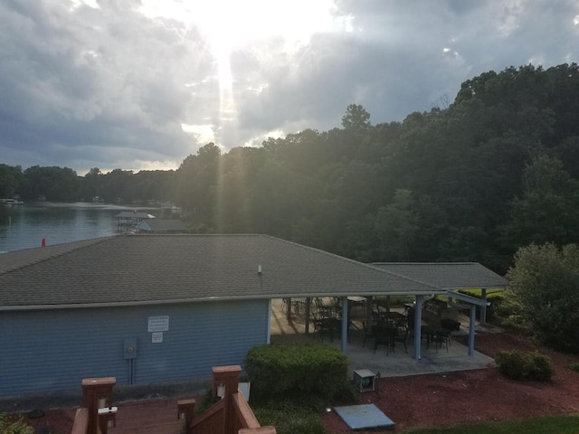 rear view of property with a patio, a water view, a shingled roof, and a forest view