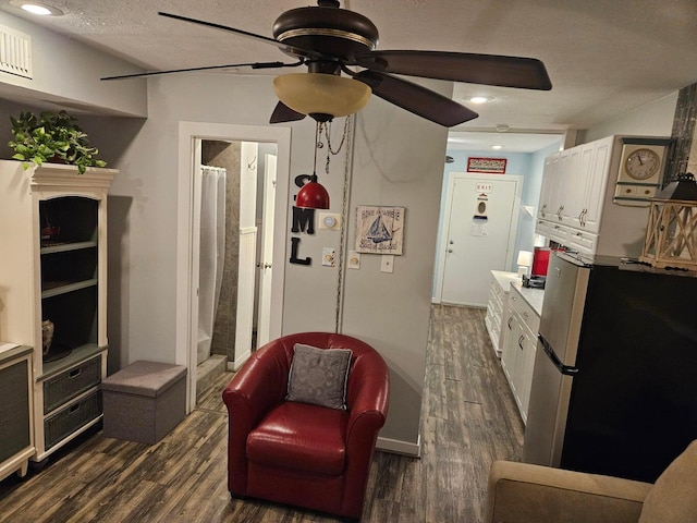 sitting room with dark wood-type flooring, a ceiling fan, a textured ceiling, and baseboards