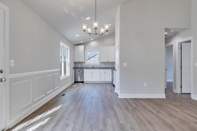kitchen with stainless steel dishwasher, an inviting chandelier, vaulted ceiling, white cabinets, and light wood-type flooring