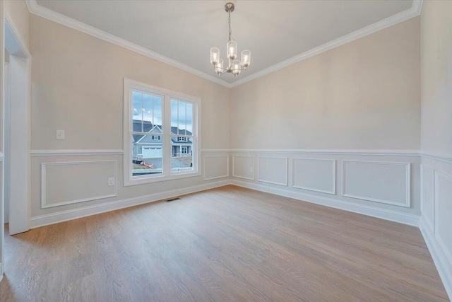 unfurnished room with crown molding, a notable chandelier, visible vents, wainscoting, and wood finished floors