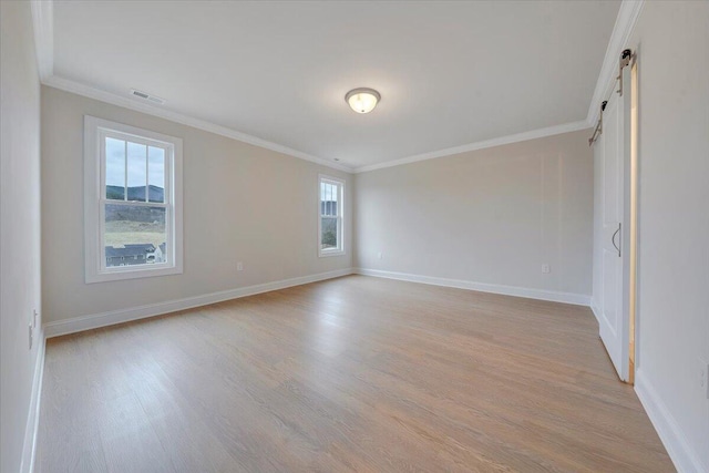 spare room with crown molding, visible vents, a barn door, light wood-style floors, and baseboards