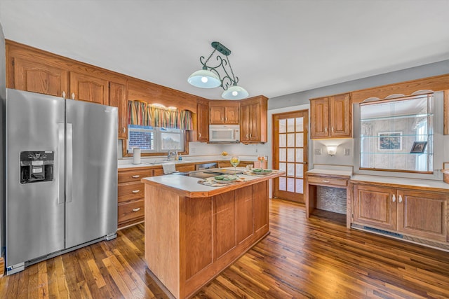 kitchen featuring brown cabinets, light countertops, white microwave, dark wood-type flooring, and stainless steel fridge