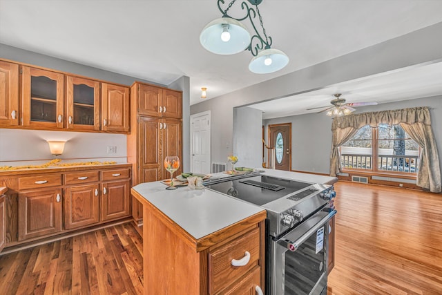 kitchen with brown cabinetry, wood finished floors, a center island, stainless steel electric stove, and light countertops