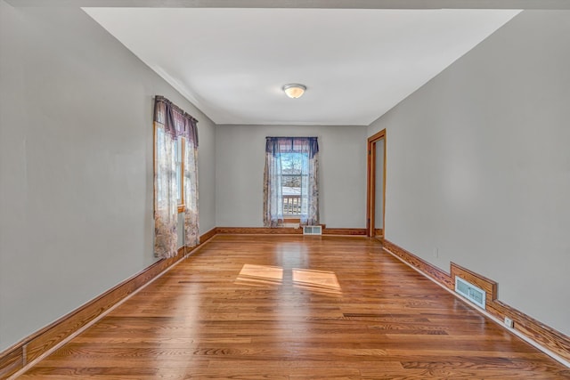 unfurnished room with wood finished floors, visible vents, and baseboards