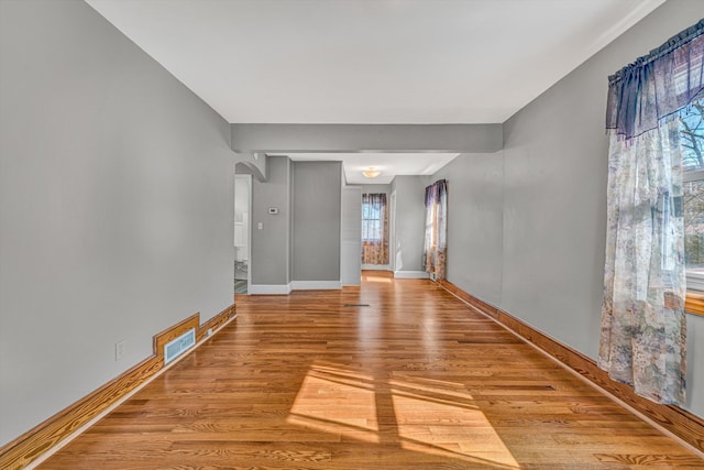 spare room with baseboards, visible vents, arched walkways, and wood finished floors